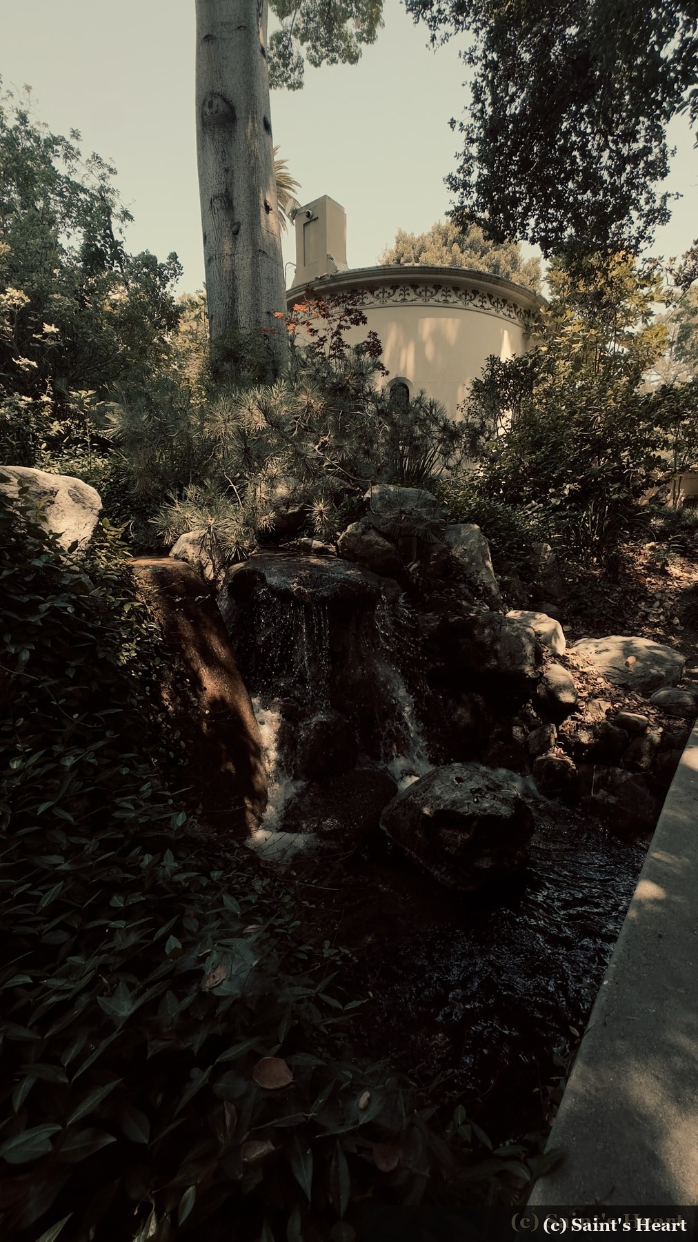 Garden waterfall beneath trees and a round building
